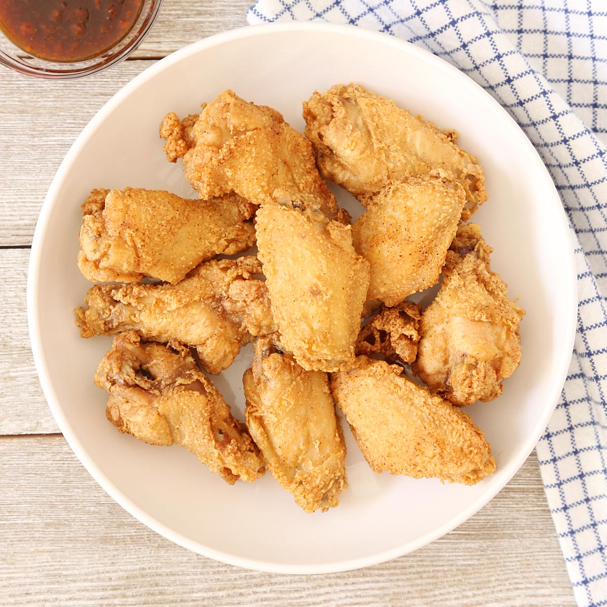 Patis fried chicken wings in a serving plate with sauce on the side.