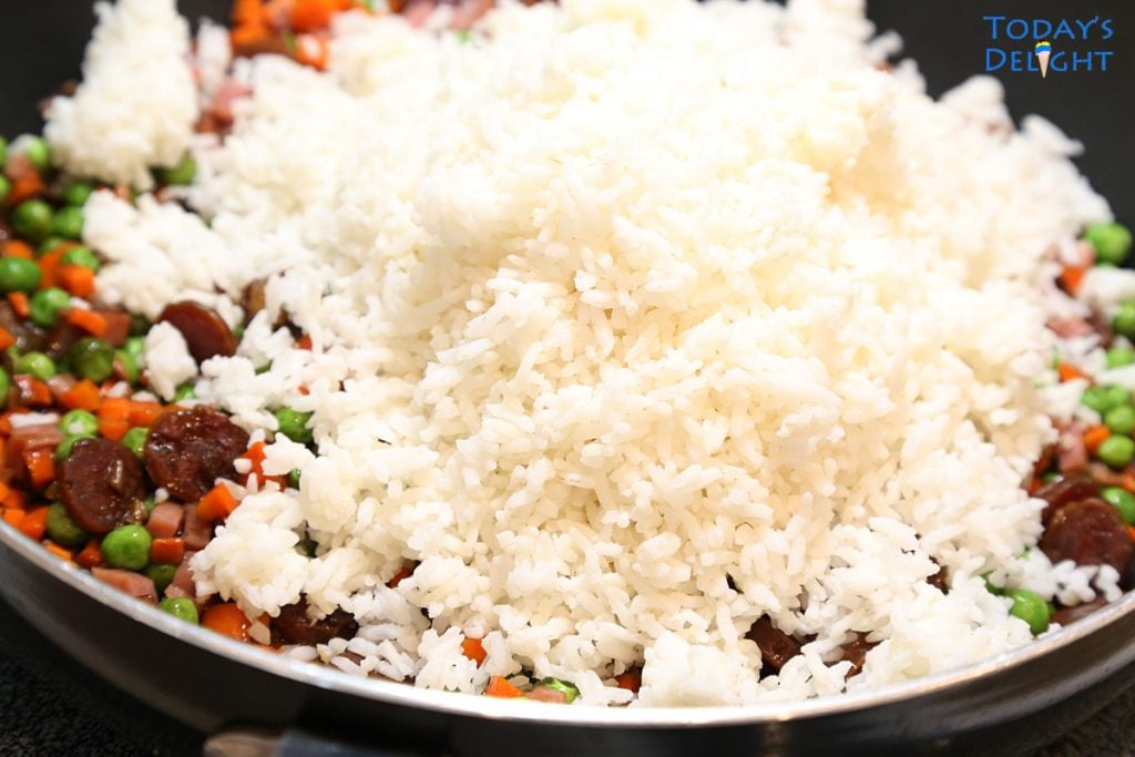 A day old white rice added to fried rice ingredients in skillet.