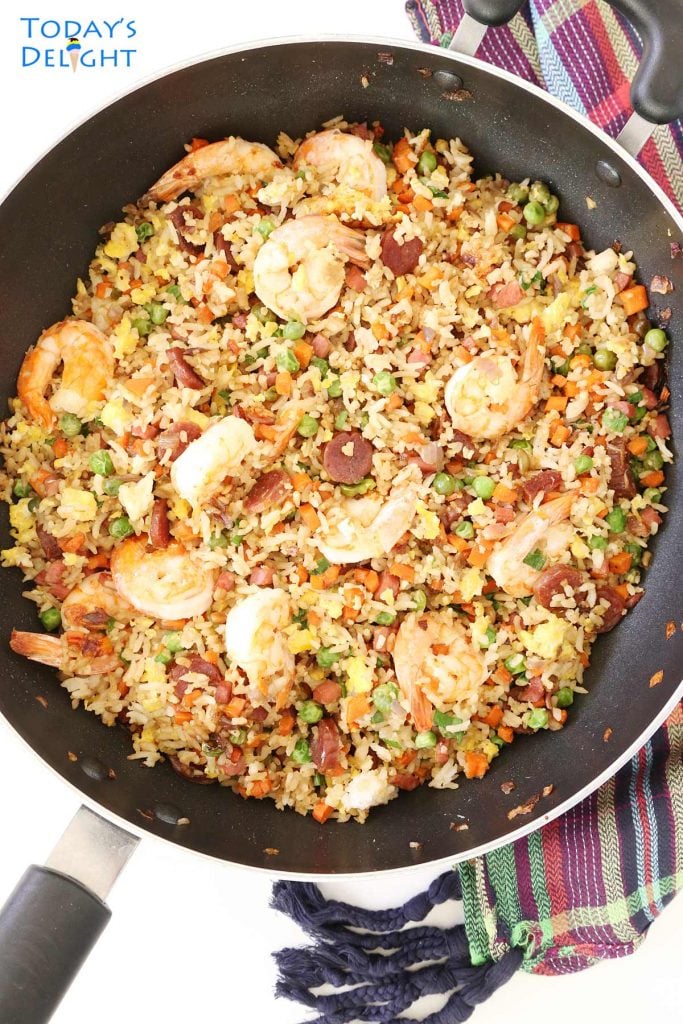 Fried rice with shrimp, ham, Chinese sausage, carrots, green peas and green onion in a skillet.