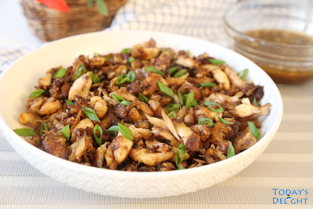 Shredded chicken adobo with chopped green onion in a serving plate with sauce on the side.