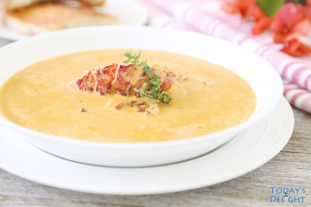 Lobster bisque soup with chunks and whole lobster and thyme as garnish with a side of French bread.