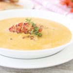 Lobster bisque soup with chunks and whole lobster and thyme as garnish with a side of French bread.