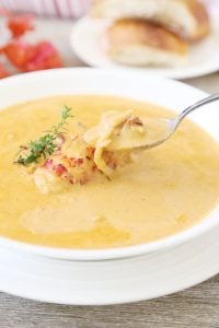 Lobster bisque soup with fresh thyme, a whole lobster tail and chunks of lobster on a spoon and a side of French bread.