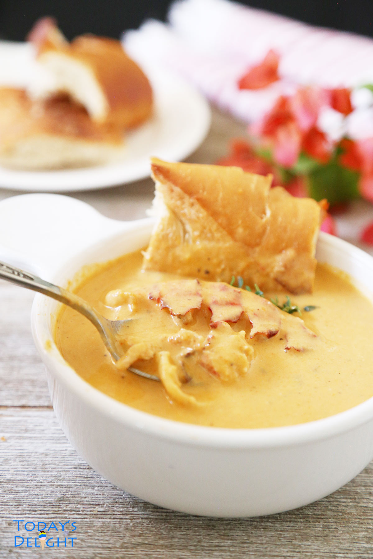 A slice of French bread dipped in lobster bisque soup and a spoonful of lobster meat and soup.