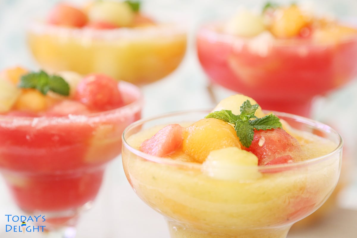 4 margarita glasses with melon balls and cubes in watermelon juice and cantaloupe-honeydew juice garnish with mint.