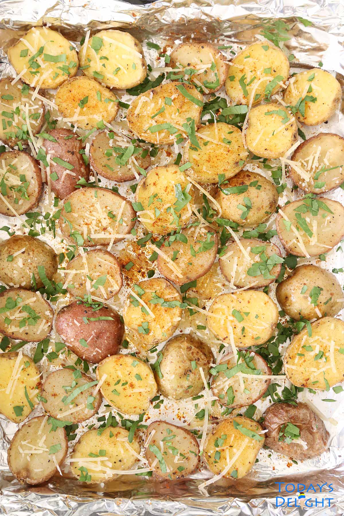 Roasted Baby Potatoes in baking pan line with foil and garnished with parmesan cheese and chopped parsley.