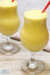 2 mango smoothie in a hurricane glass with red straws.