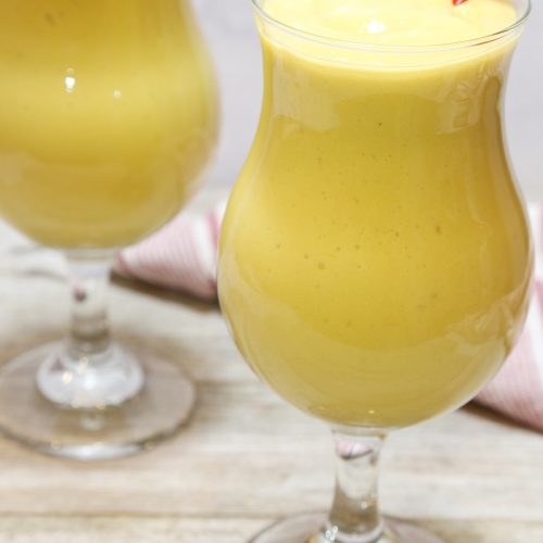 2 mango smoothie in a hurricane glass with red straws.