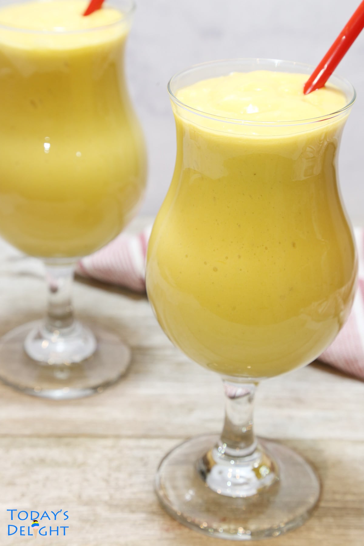2 mango smoothie in a hurricane glass with red straws.