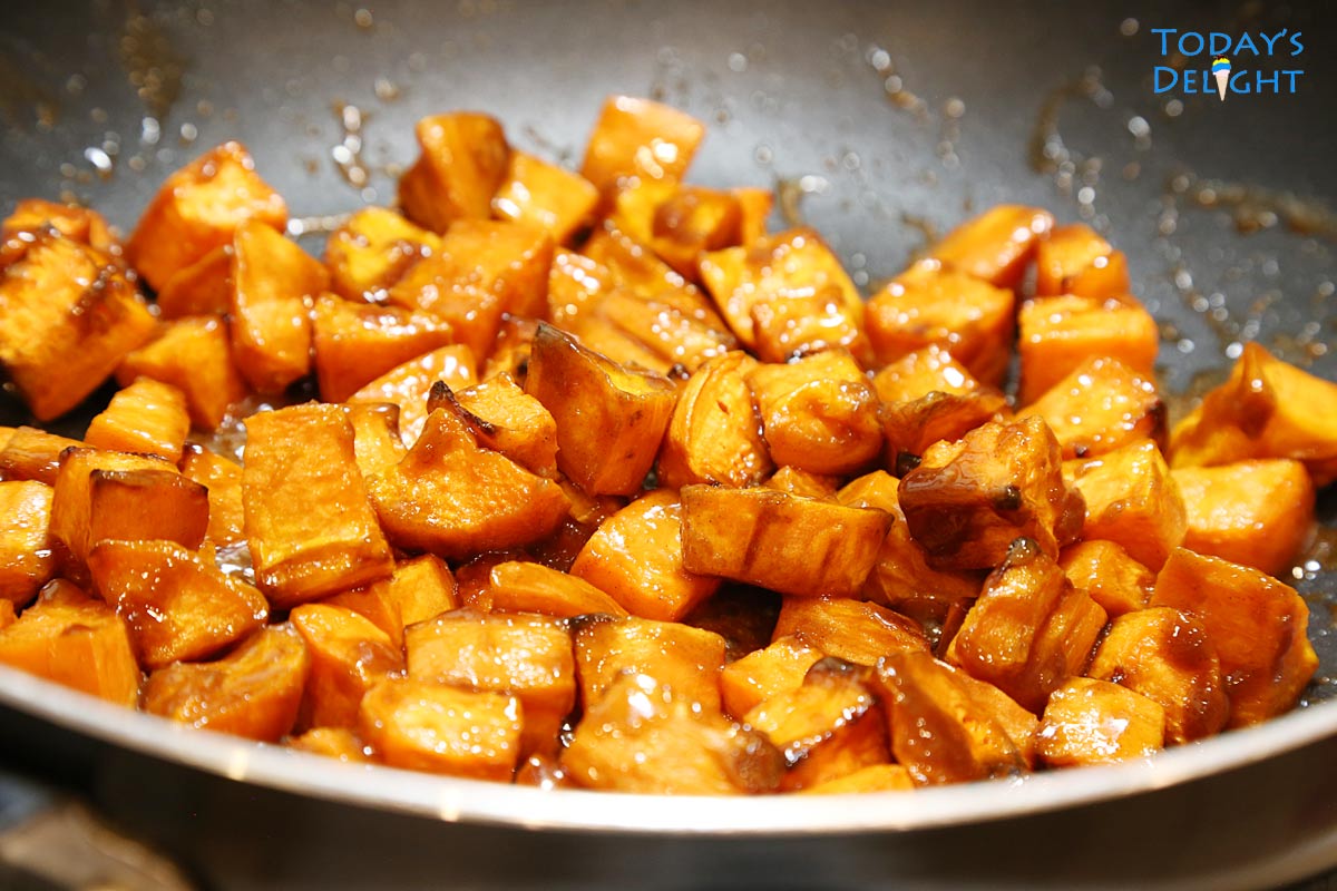 Roasted sweet potatoes stirred-in with sugar glaze in pan.