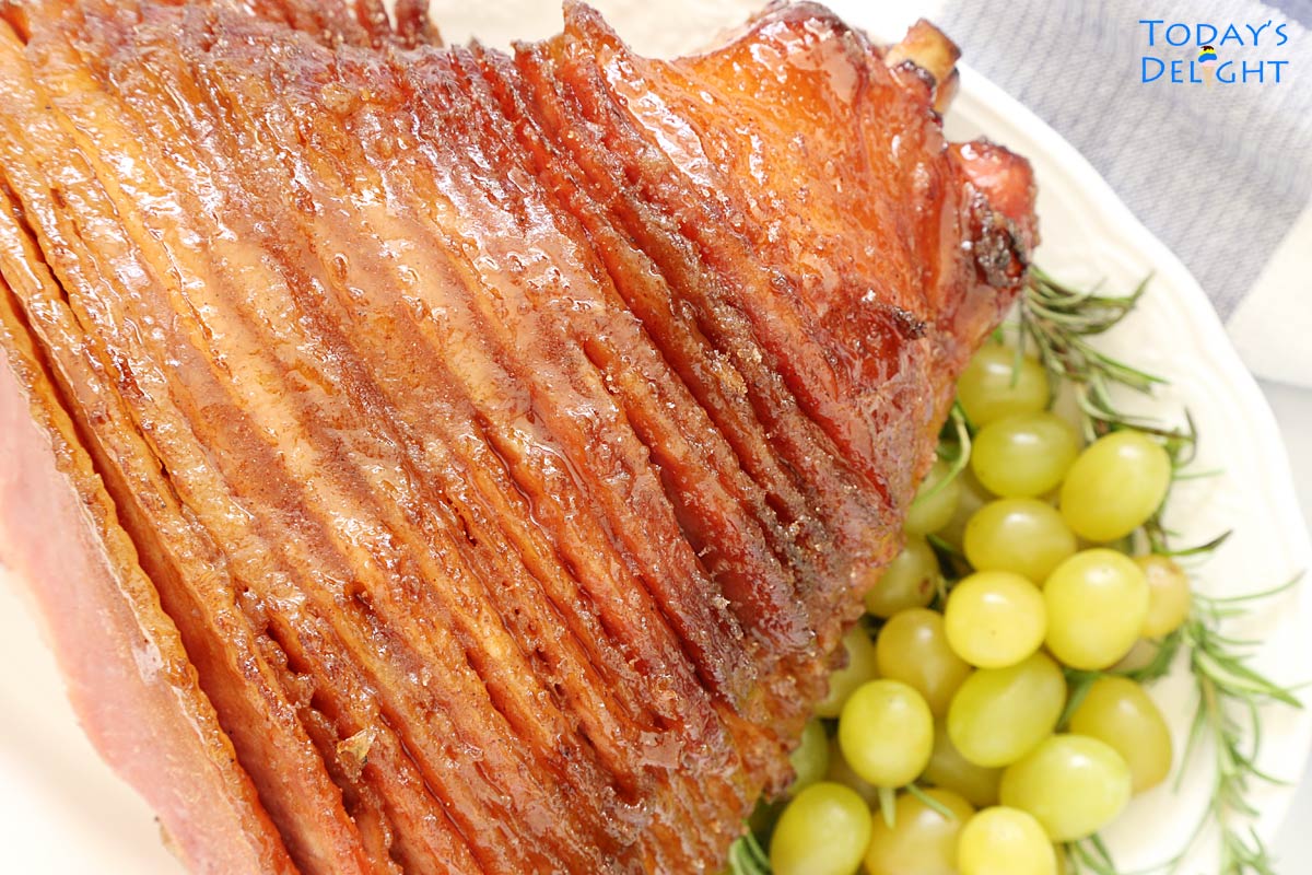 Hone baked spiral cut ham on a platter decorated on the side with fresh rosemary and green grapes.