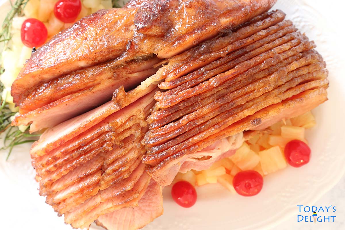 Pineapple honey glazed spiral cut ham on a platter with fresh rosemary, cherries and pineapple.