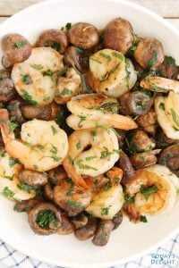 Peeled shrimp and mushroom with cilantro and parsley in a serving plate.
