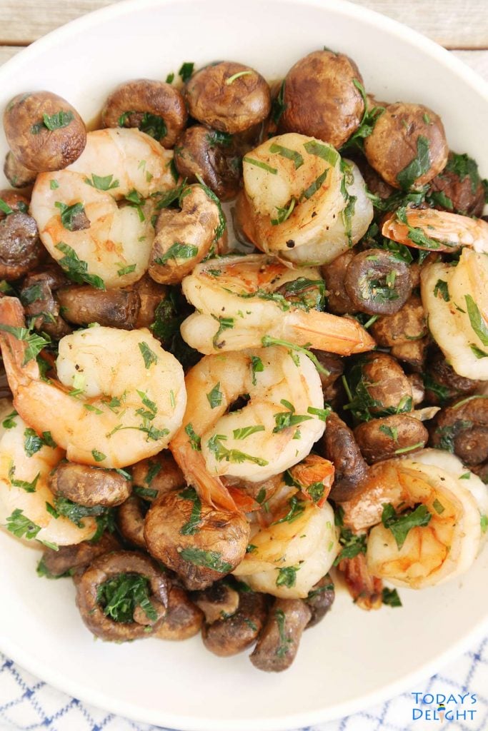 Peeled shrimp and mushroom with cilantro and parsley in a serving plate.