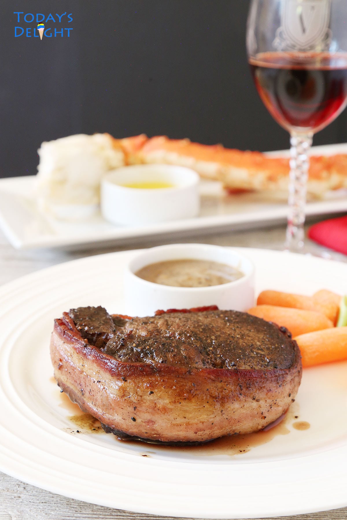Filet mignon wrapped in bacon with mushroom sauce and baby carrots on the side and crab legs. 