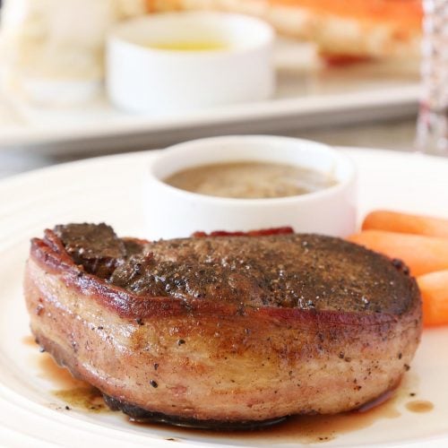 Bacon wrapped filet mignon with sides of mushroom sauce and carrots and crab leg.