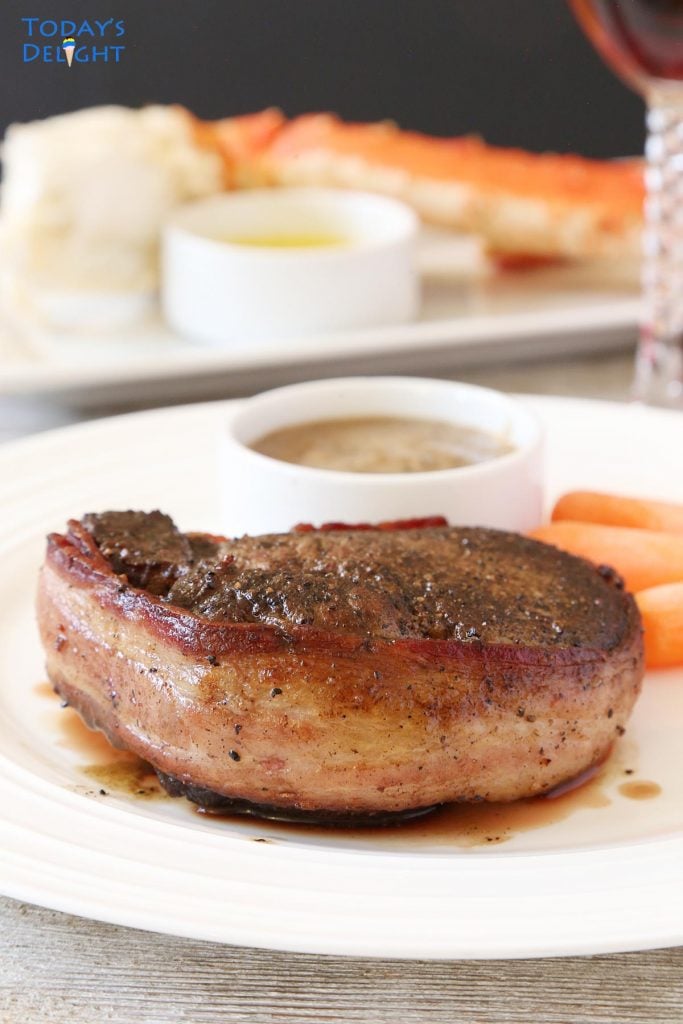 Bacon wrapped filet mignon with sides of mushroom sauce and carrots and crab leg.