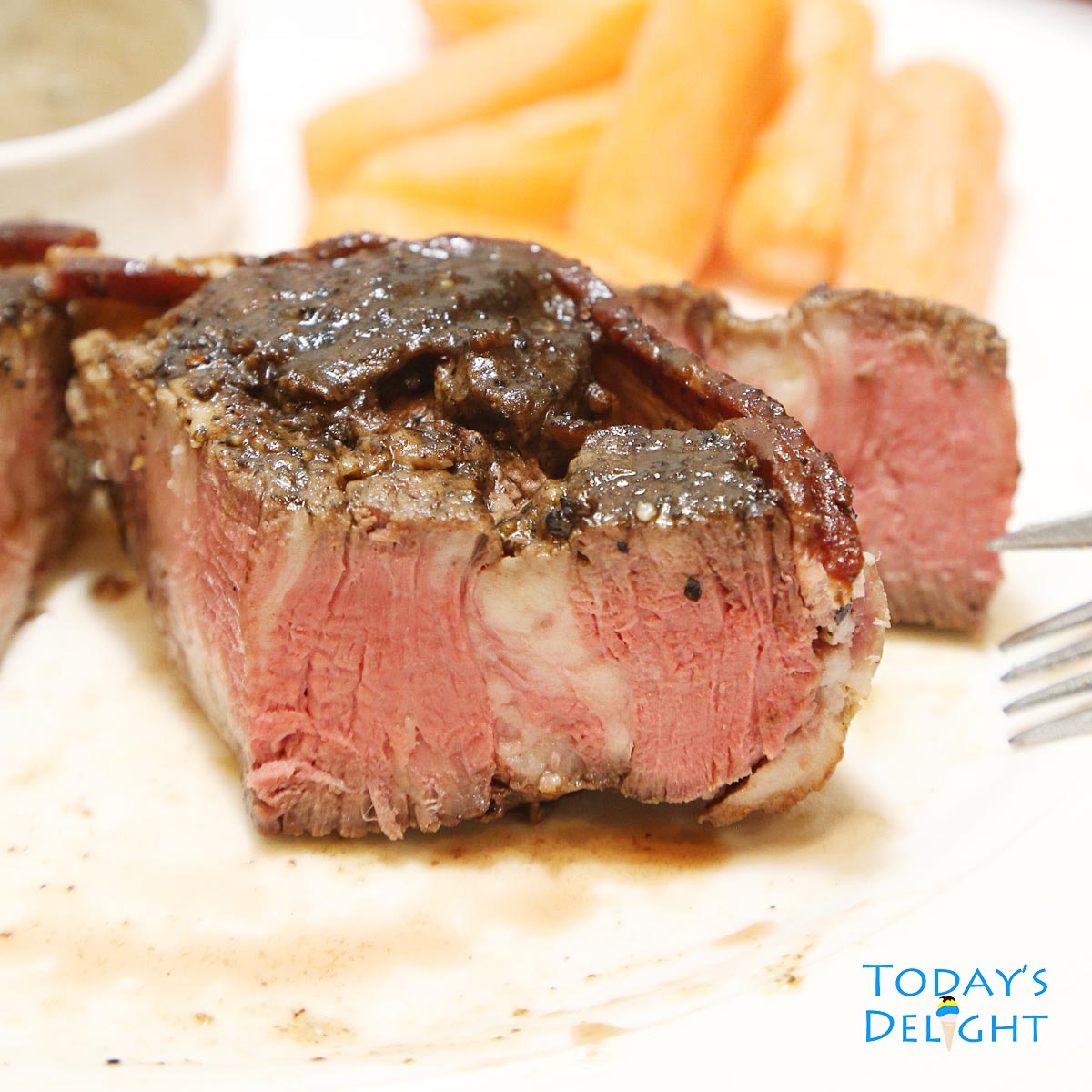 Sliced filet mignon cooked to medium doneness with mushroom sauce and baby carrots on the side.