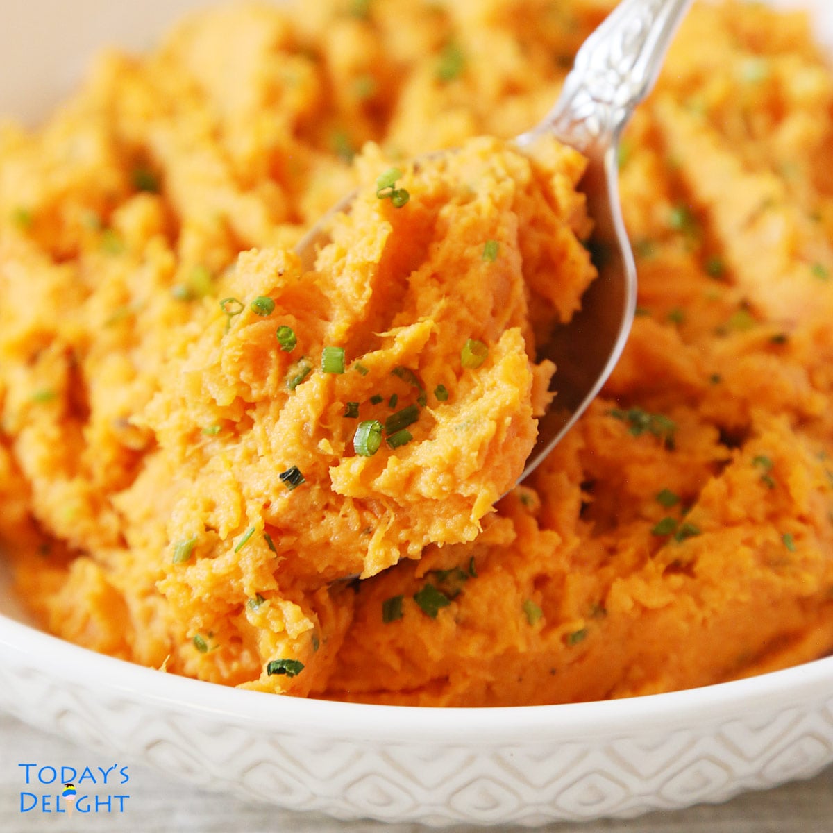 A spoonful of mashed sweet potatoes and served in a shallow serving bowl.