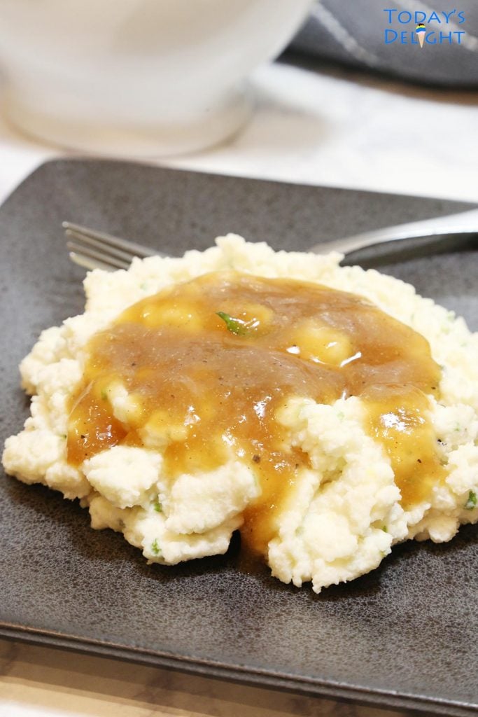 Mashed potatoes with beef broth brown gravy on a plate and a sauce dish.