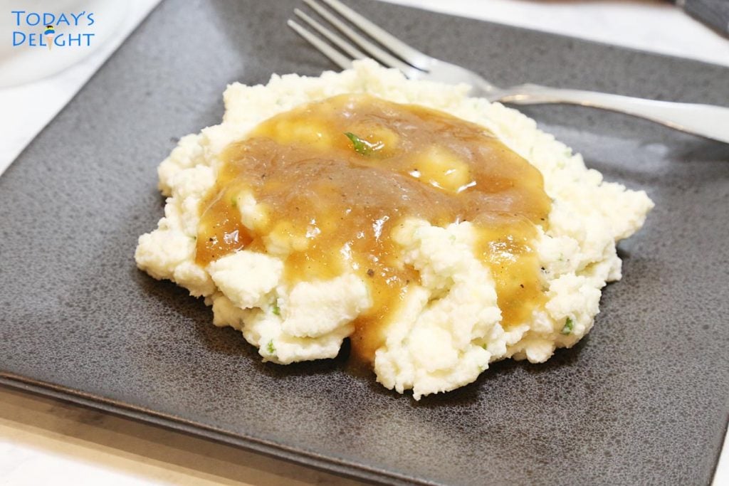 Mashed potatoes with brown gravy on a plate.