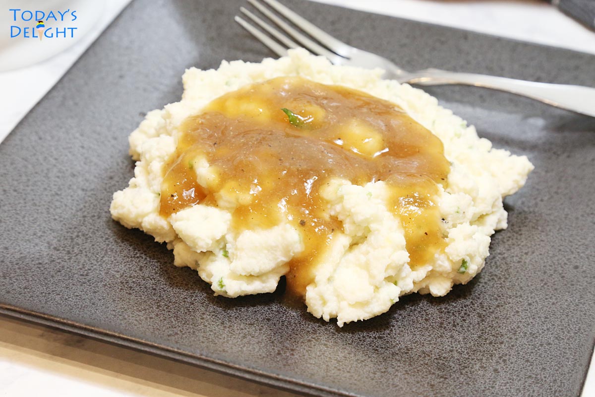 Mashed potatoes with brown gravy on a plate.