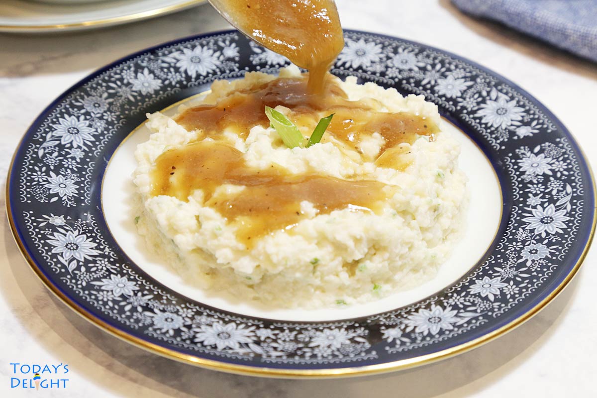 Mashed potatoes on a plate with brown gravy.