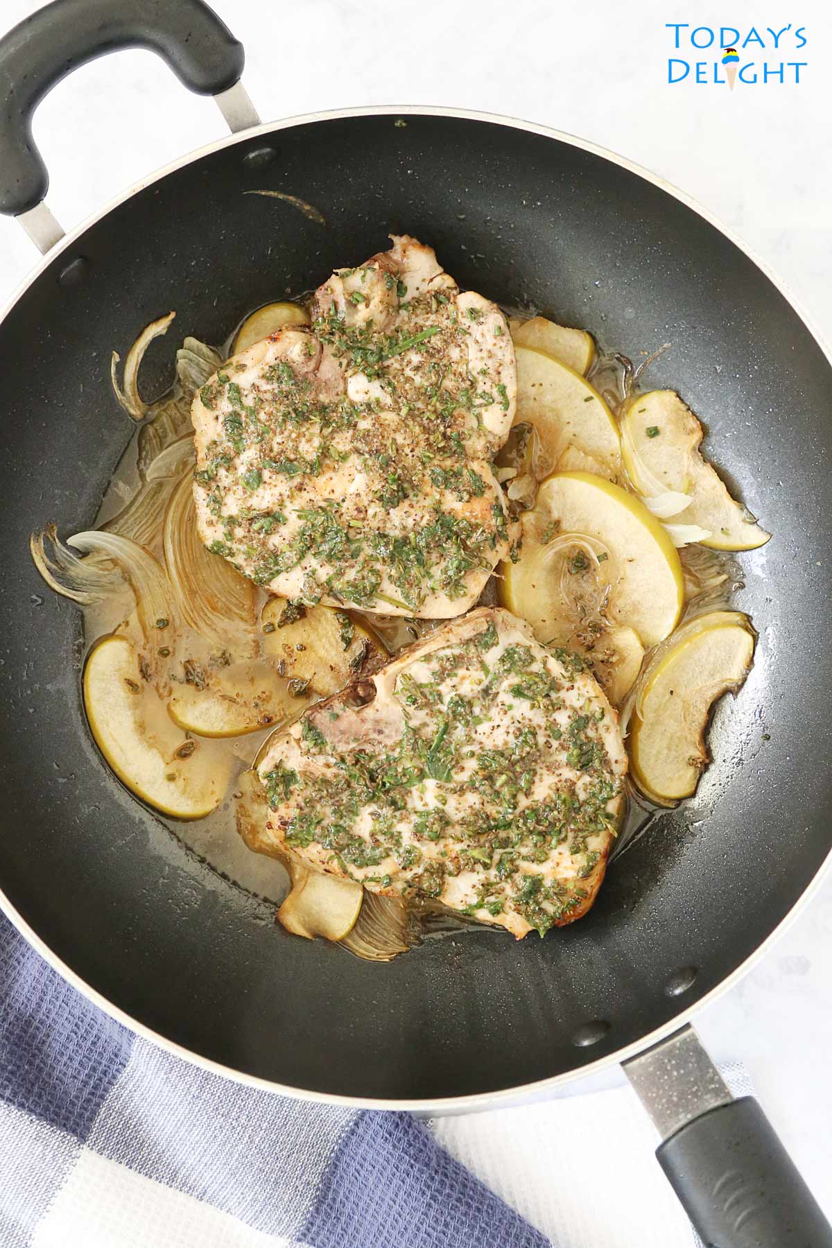 Two herb pork chops with apples and onions in a skillet.