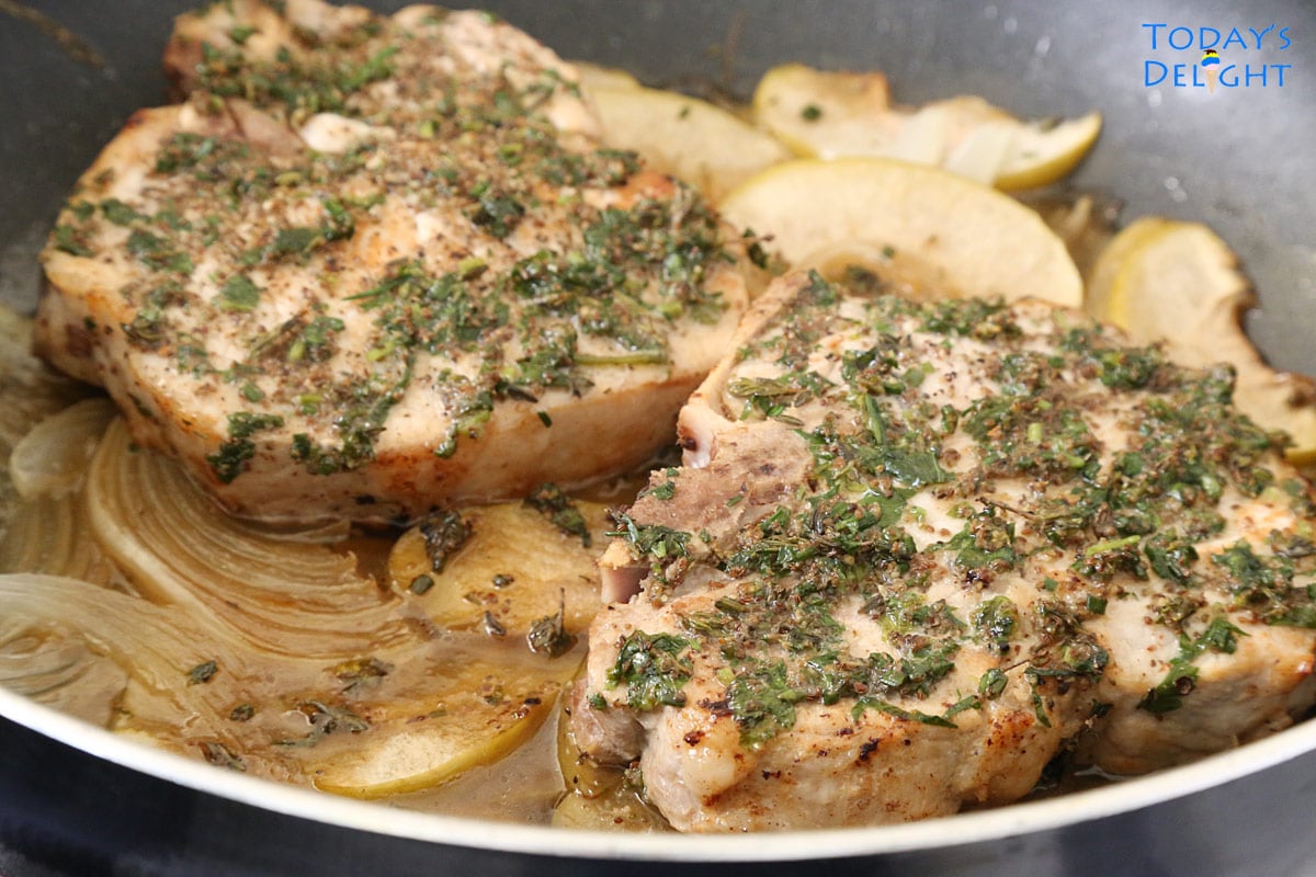 Two herb center cut pork chops cooked in apples and onions in a skillet.