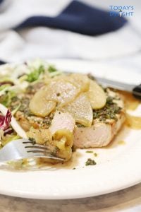 Sliced pork chop topped with apples and onions and a side of salad on a plate.