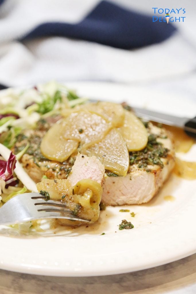 Sliced pork chop topped with apples and onions and a side of salad on a plate.