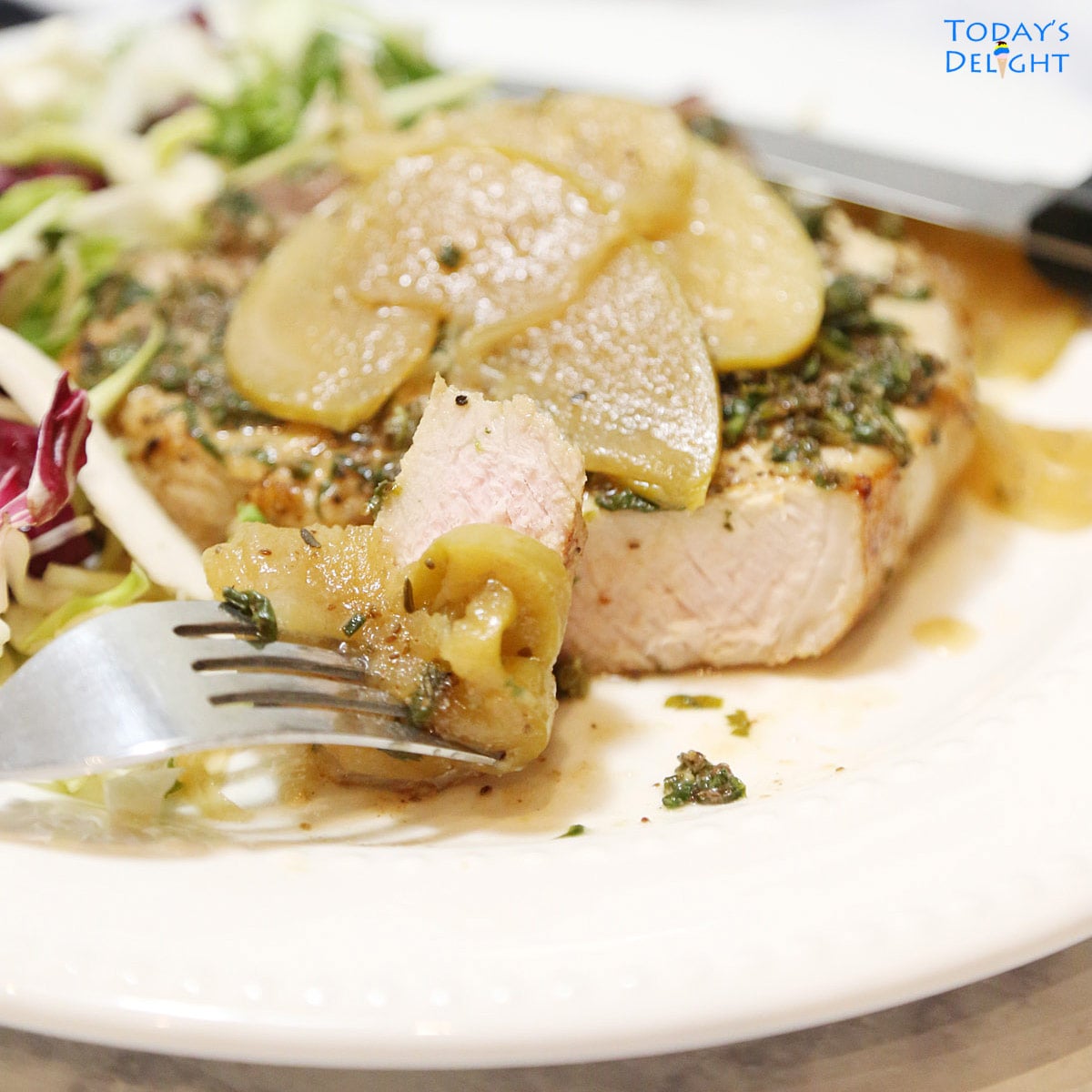 Sliced pork chop topped with cooked apple and salad on the side.