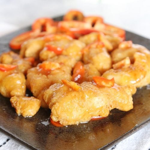 Air fryer orange chicken with red bell peppers on a plate.