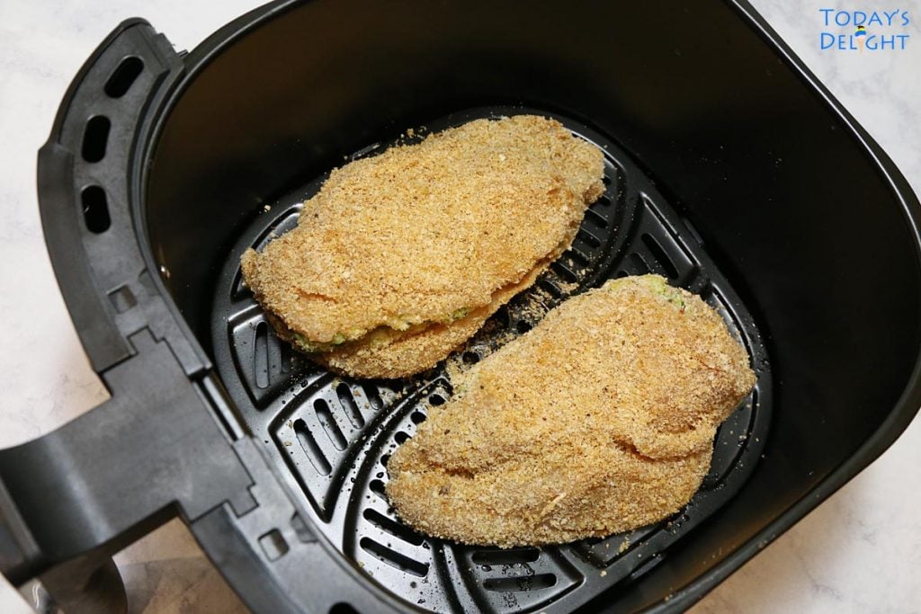 Two raw stuffed chicken breast with broccoli and cheese in an air fryer basket.