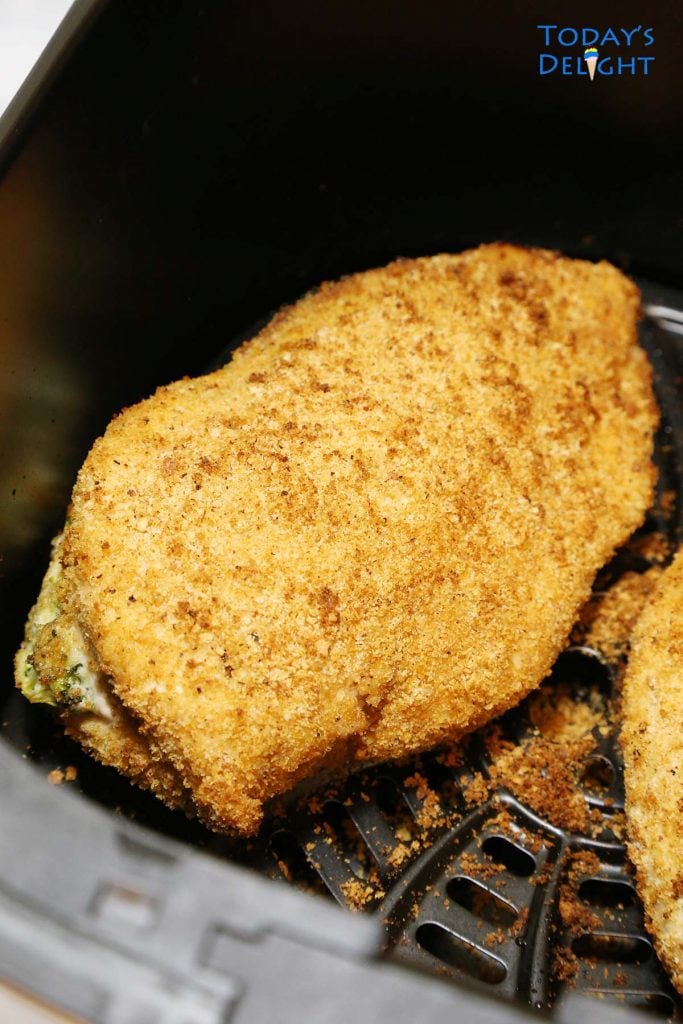 Two cooked air fryer stuffed chicken breast with broccoli and cheese in basket.