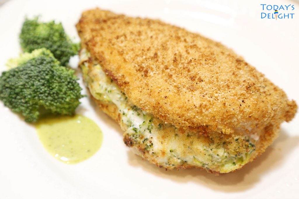 Chicken breast filled with broccoli cheese mixture on a plate with a side of broccoli and sauce.