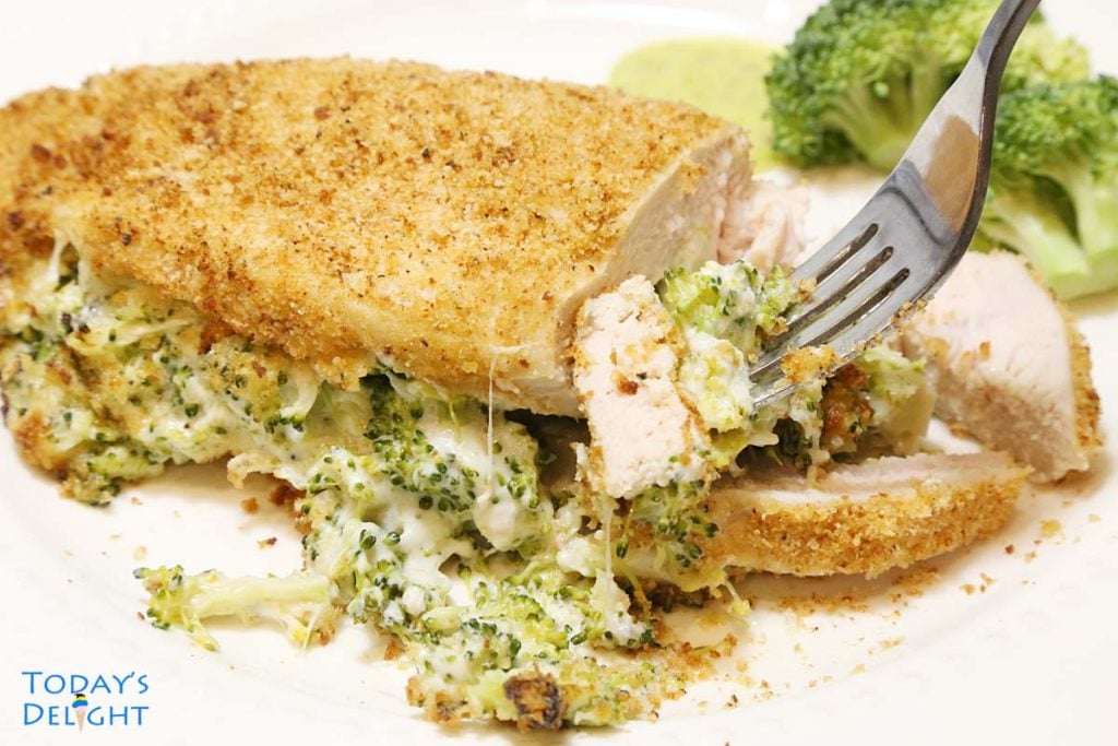 Cooked sliced chicken breast with broccoli cheese filling in a fork.