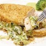Cooked sliced chicken breast with broccoli cheese filling in a fork.