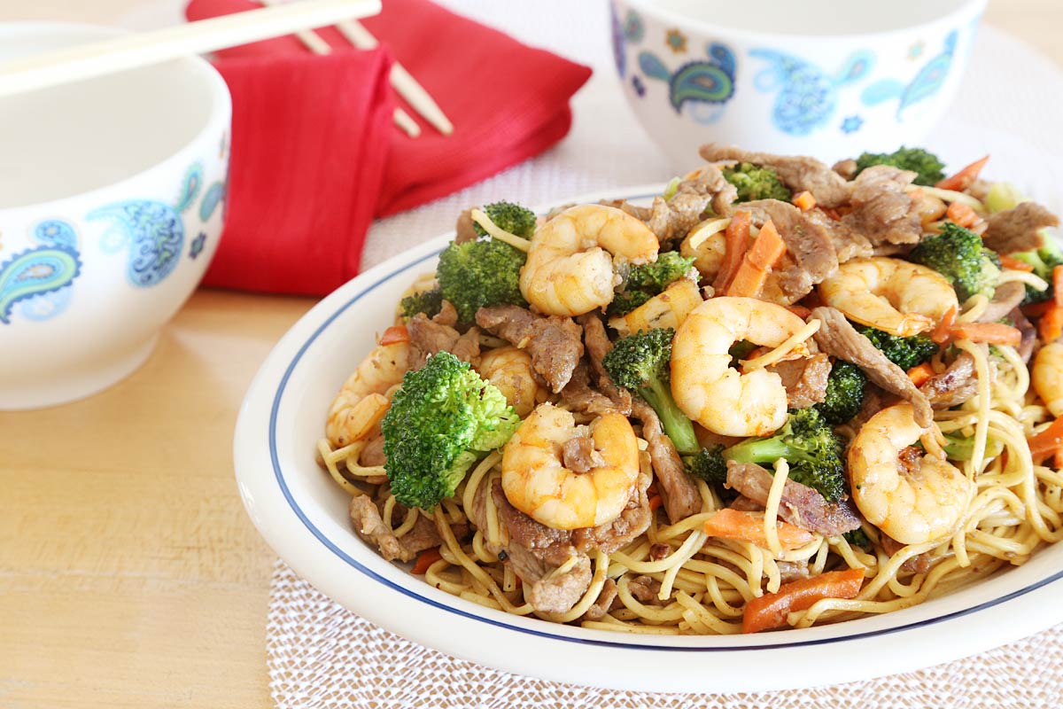 Pork, vegetable, shrimp lo mein in a serving platter with 2 bowls, red napkins and chop sticks on the side.