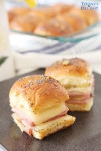 Two ham and cheese sliders on a plate and more in baking pan.