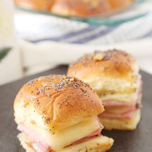 Two ham and cheese sliders on a plate and more in baking pan.