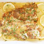 Baked cod in garlic butter sauce garnished with parsley and surrounded with lemon slices.