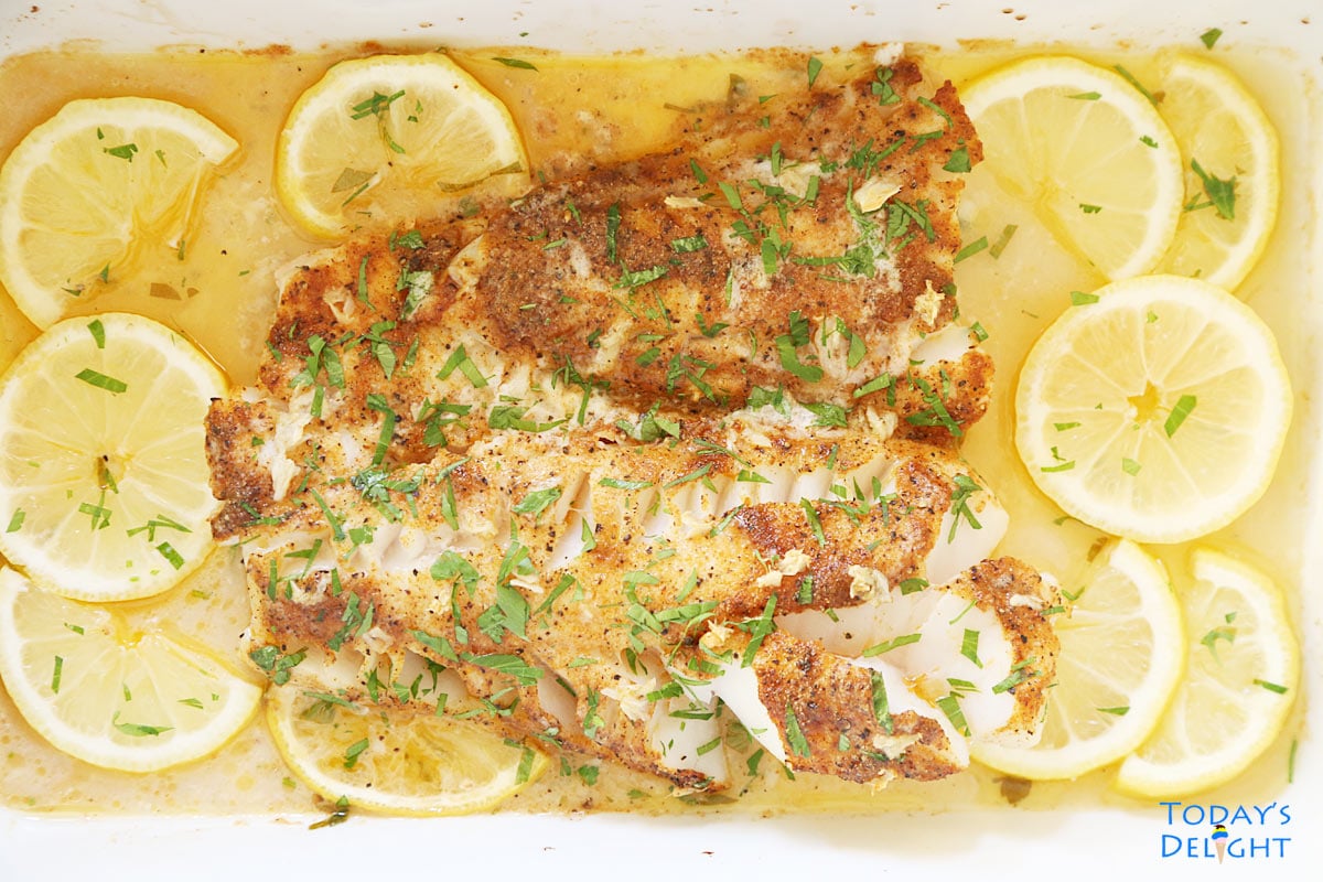 Baked cod in garlic butter sauce garnished with parsley and surrounded with lemon slices.
