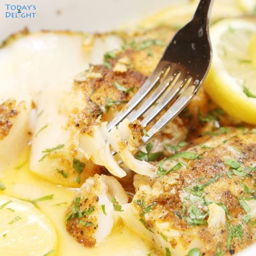Flaky baked cod in fork and casserole garnish with parsley with sauce and sliced lemon.