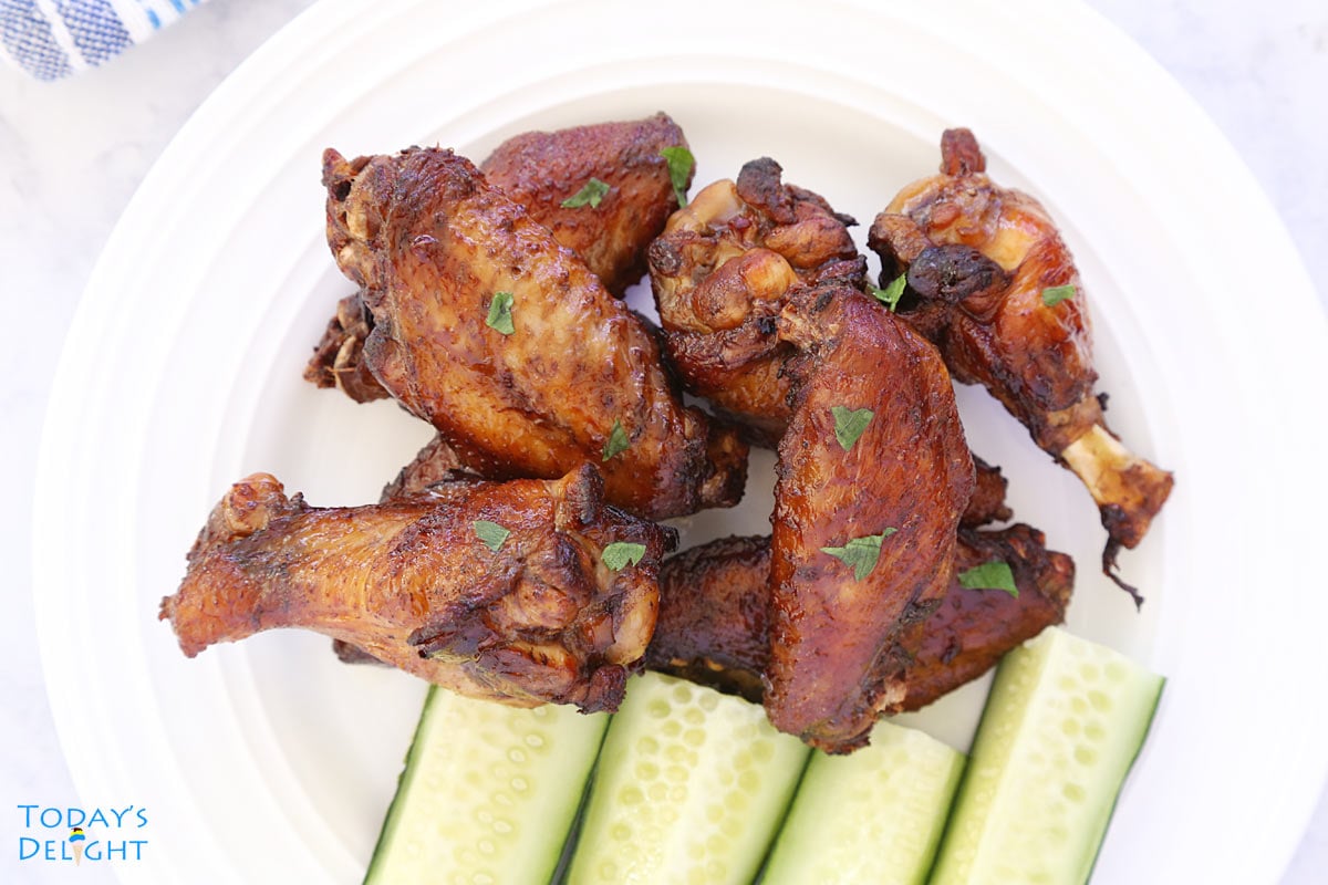 Chicken wings both drummettes and flats with a side of sliced cucumbers on a plate.