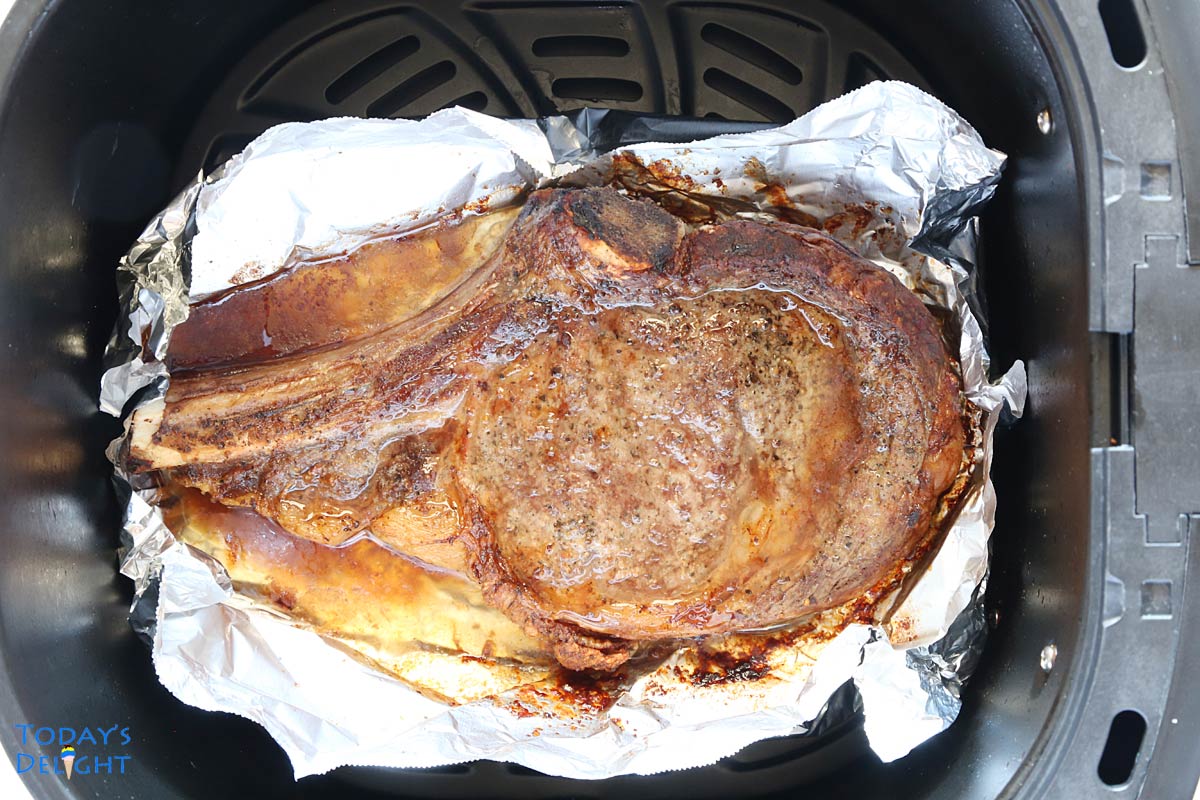 One cooked bone-in ribeye steak lined with foil in air fryer basket.