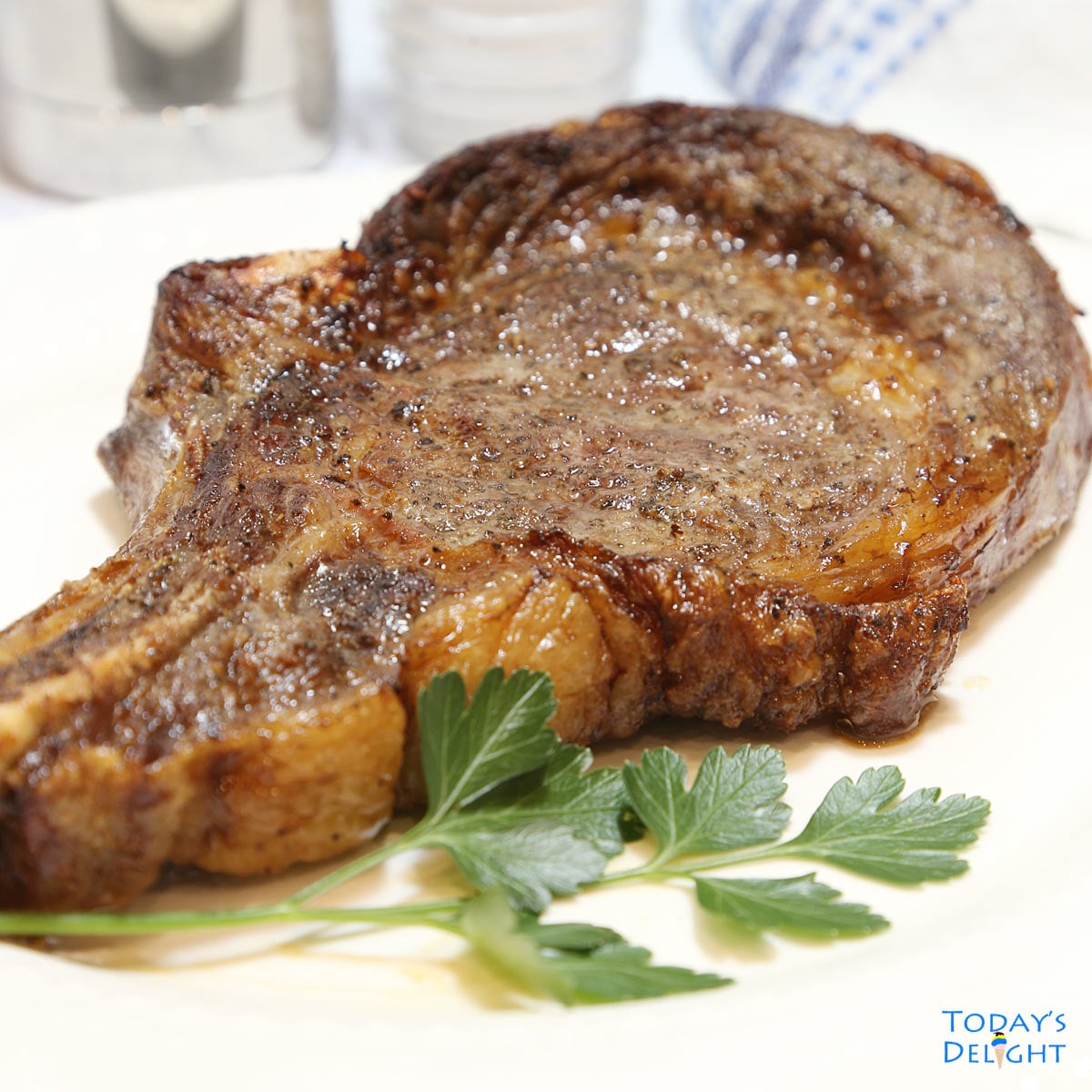 Plated air fried ribeye steak with parsley leaves as garnished and salt and pepper on the side.
