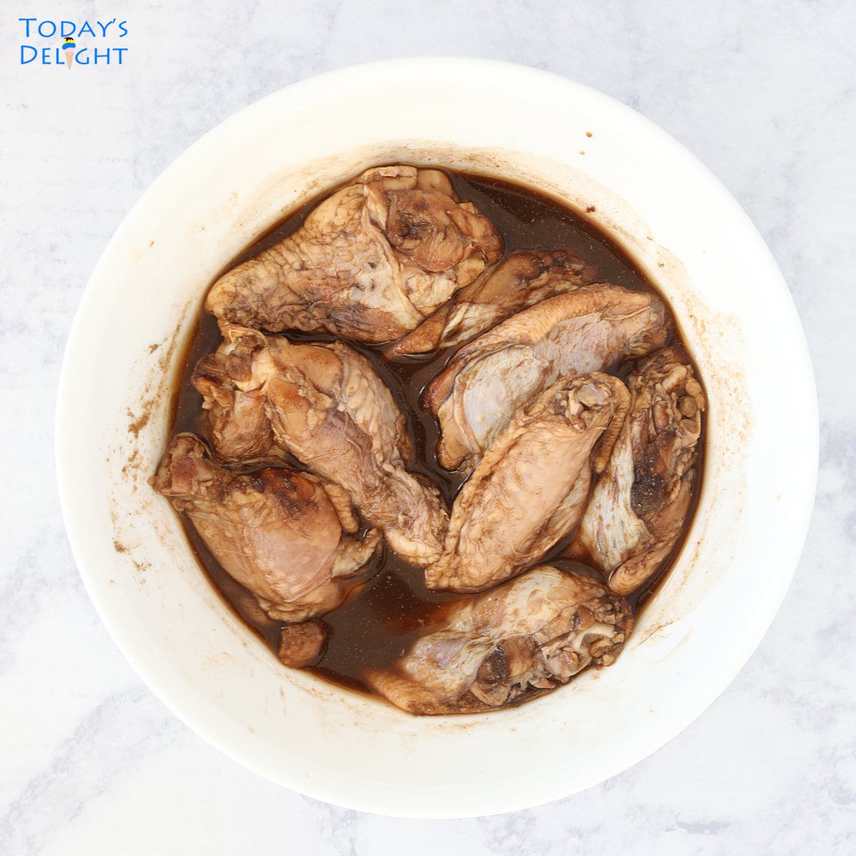 Chicken wings in a big bowl submerged in marinade ingredients.