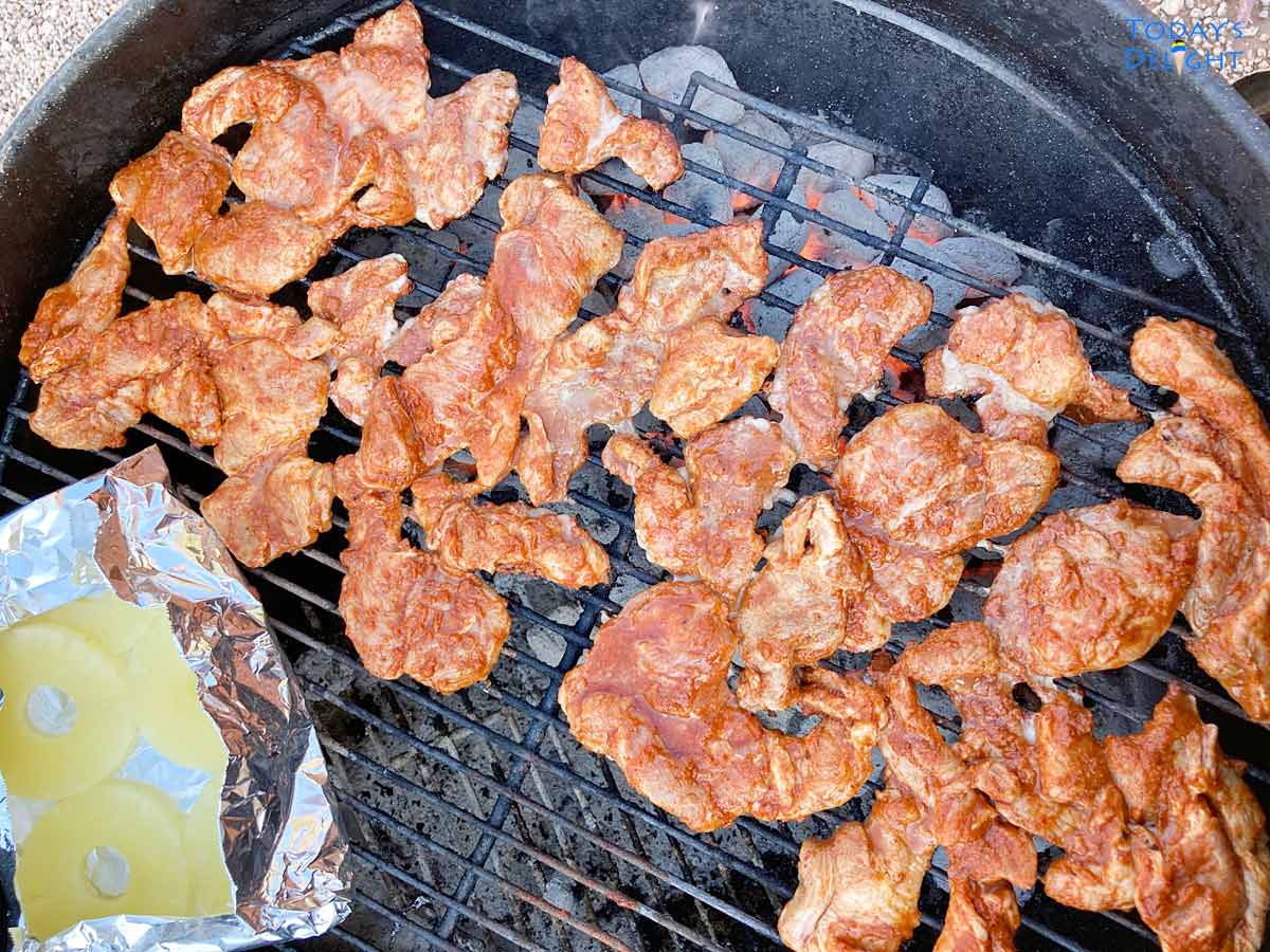 Grilling al pastor pork and pineapple slices in charcoal.