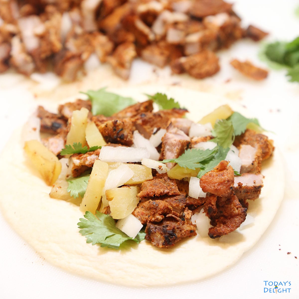 Assemble al pastor tacos with warm tortilla, grilled pork and pineapple, cilantro and onion.